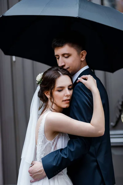 一起在一把黑色的伞下 恋爱中的年轻夫妇 新娘有一头乌黑的头发和长长的面纱 新娘花束 — 图库照片