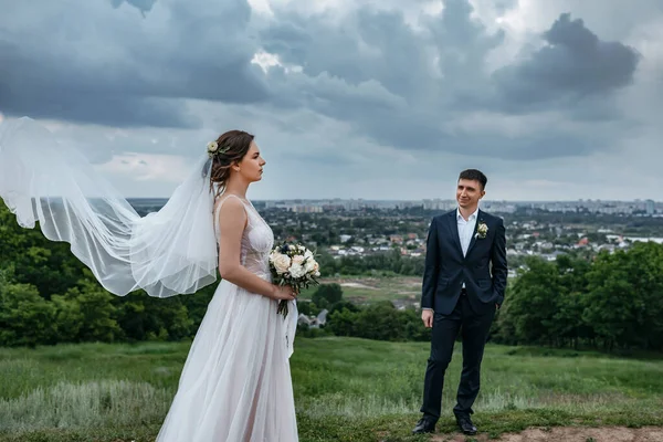 新娘和新郎在乌云密布的天空中 美丽的面纱在风中飘扬 — 图库照片