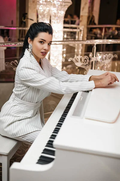 迷人的黑发姑娘穿着白色西服坐在一架白色钢琴前 华丽的气氛奢华的细节 — 图库照片