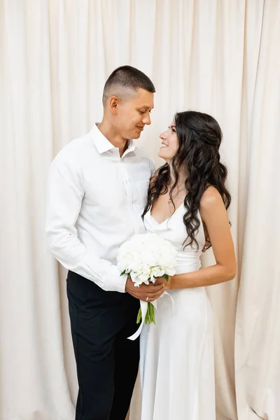 白いカーテンの前でポーズをとる笑顔の結婚式のカップル — ストック写真