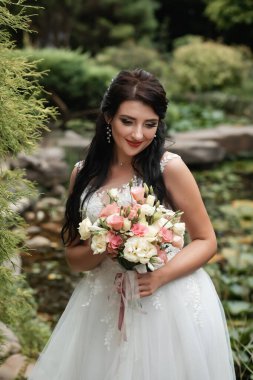 Güzel botanik parkında poz veren büyük bir düğün buketiyle mutlu bir gelin..