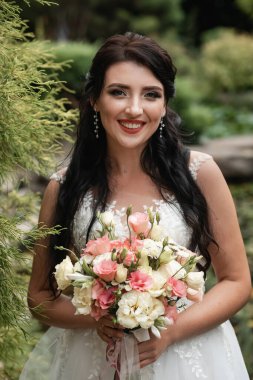 Güzel botanik parkında poz veren büyük bir düğün buketiyle mutlu bir gelin..