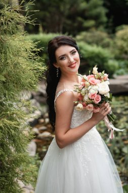 Güzel botanik parkında poz veren büyük bir düğün buketiyle mutlu bir gelin..