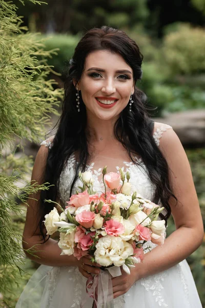 Güzel botanik parkında poz veren büyük bir düğün buketiyle mutlu bir gelin..