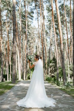 Çam ormanında elinde güzel bir buketle poz veren Avrupalı bir gelin..