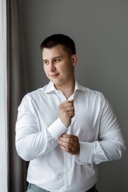 Beyaz gömlekli çekici bir damat pencerenin yanında poz veriyor. Doğal ışık