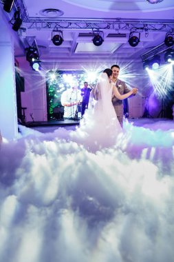 Düğün çifti dans ediyor, etraflarında dumanlar yükseliyor. Pembe ve mavi ışıklar