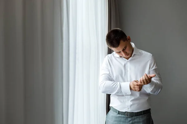Beyaz gömlekli çekici bir damat pencerenin yanında poz veriyor. Doğal ışık