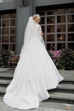 Şehir caddesinde uzun ve zarif bir duvağı olan şık bir gelin. Sırtında duruyorum..