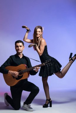 Akustik gitarlı siyah takım elbiseli neşeli bir gitarist. Siyah elbiseli hoş bir kız. Renkli arkaplan