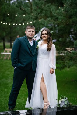 Kıvrımlı insanlar, yürüyüş yapan bir çift. Zarif bir gelin, yeşil takım elbiseli bir damat. Güzel park
