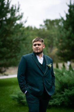 Havuzun önünde yeşil takım elbiseli şık bir adam ve yeşil parktaki bir ev. Bulanık bir çelenk.