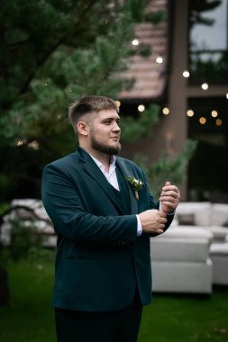 Havuzun önünde yeşil takım elbiseli şık bir adam ve yeşil parktaki bir ev. Bulanık bir çelenk.