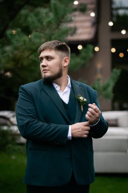 Havuzun önünde yeşil takım elbiseli şık bir adam ve yeşil parktaki bir ev. Bulanık bir çelenk.