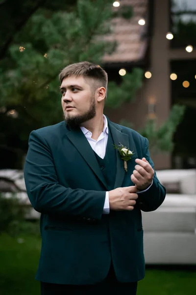 Havuzun önünde yeşil takım elbiseli şık bir adam ve yeşil parktaki bir ev. Bulanık bir çelenk.