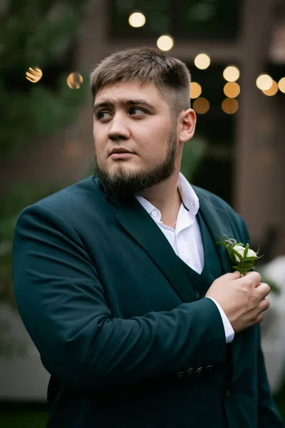 Havuzun önünde yeşil takım elbiseli şık bir adam ve yeşil parktaki bir ev. Bulanık bir çelenk.