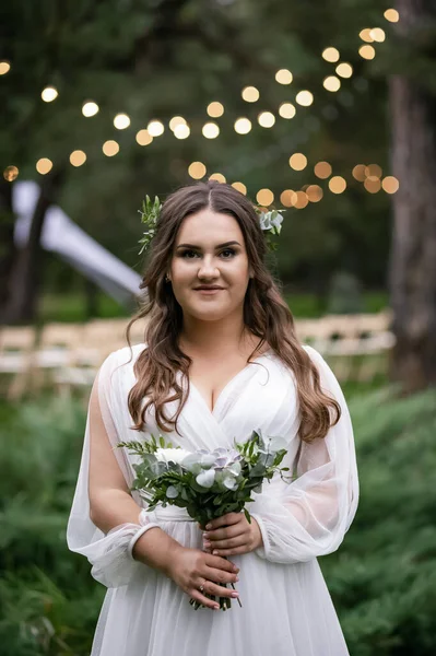 Beyaz gelinlikli ayyaş kız. Zarif, çekici ve neşeli bir gelin. Arka planda ampuller olan yeşil park.