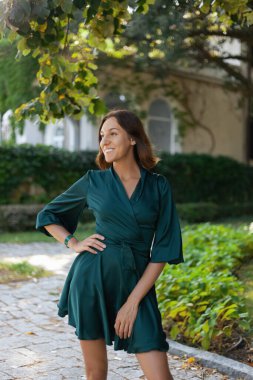 Turkuaz bir elbiseyle gülümseyen, sofistike bir kız iyi korunmuş yeşil bir parkta yürüyor. Tropikal bir ülkede sıcak bir yaz.. 