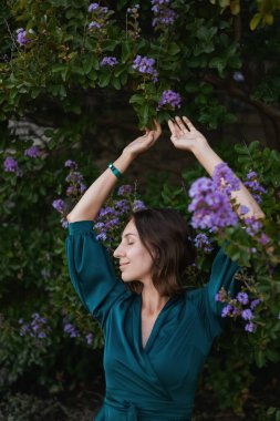 Turkuaz bir elbiseyle gülümseyen, sofistike bir kız iyi korunmuş yeşil bir parkta yürüyor. Tropikal bir ülkede sıcak bir yaz.. 