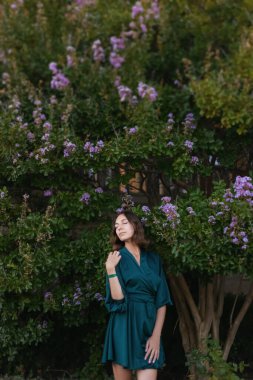 Turkuaz bir elbiseyle gülümseyen, sofistike bir kız iyi korunmuş yeşil bir parkta yürüyor. Tropikal bir ülkede sıcak bir yaz.. 