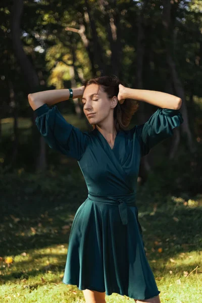 A smiling, sophisticated girl in a turquoise light dress walks in a well-kept green park. It's a hot summer in a tropical country.