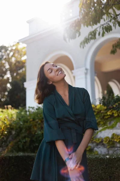 A smiling, sophisticated girl in a turquoise light dress walks in a well-kept green park. It's a hot summer in a tropical country.