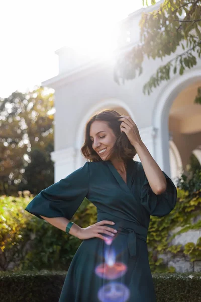 A smiling, sophisticated girl in a turquoise light dress walks in a well-kept green park. It\'s a hot summer in a tropical country.