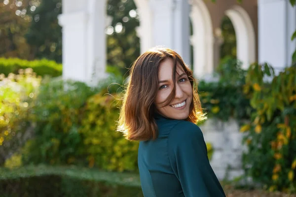 A smiling, sophisticated girl in a turquoise light dress walks in a well-kept green park. It's a hot summer in a tropical country.