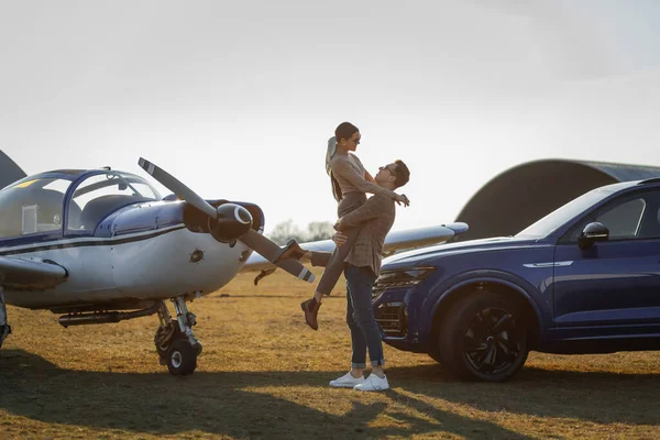 日落在机场 蓝色的吉普和飞机 漂亮时髦的一对富有的夫妇 买车时的快乐心情 免版税图库照片