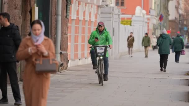 Moscú, Rusia-noviembre de 2021: Un mensajero en mono verde en una bicicleta va a entregar comida en el otoño. quitado de las manos — Vídeo de stock
