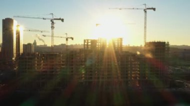 Gün batımında yeni bir yerleşim tesisinde ev inşa etme sürecinde olan çok sayıda inşaat kulesi vinci. Hava görünümü