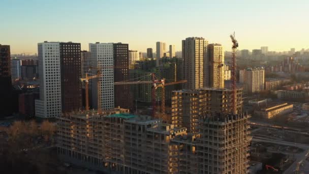 Vários guindastes de torre de construção no processo de construção de casas em um novo complexo residencial ao pôr do sol. Vista aérea — Vídeo de Stock