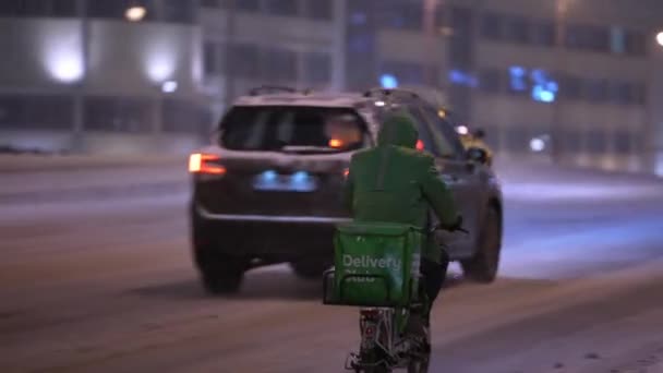 Moskva, Ryssland - december 2021: Kurir på natten på vintern på en cykel på vägen under snöfall. Kurir med cykel på vintern — Stockvideo