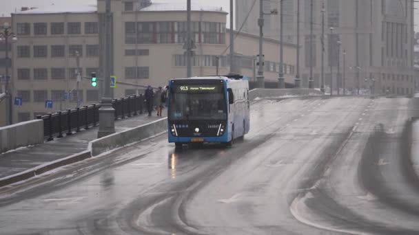 Moscou, Rússia - dezembro de 2021: Um ônibus urbano moderno azul segue a rota durante a queda de neve. Movimento lento — Vídeo de Stock
