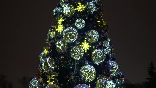Рождественские светящиеся игрушки на городской елке вечером в городе. Close up — стоковое видео