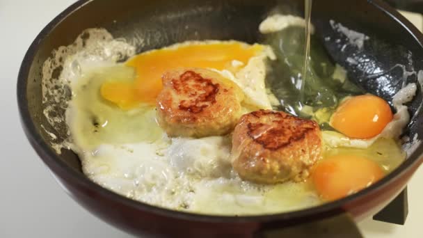 Due cotolette di pollo sono fritte con uova in olio d'oliva in una padella nera di Teflon. Rallentatore — Video Stock