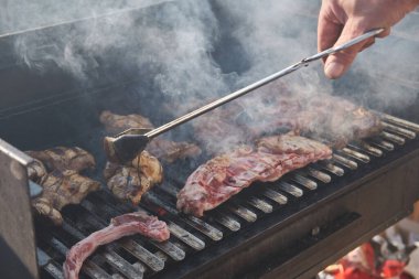 Açık hava partisi için barbekü ızgarasında pirzola pişiren bir adam. Mangal dumanı. Gıda arkaplanı.