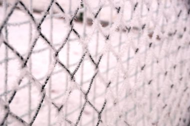 Okul bahçesinin çitlerinde karla kaplı ağlar var.                               