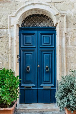 Malta inanılmaz derecede eşsiz kapılara ev sahipliği yapıyor. Vallet 'te geleneksel renkli Malta kapıları. Malta' dan ev kapı dolaşarak. Mavi ahşap kapı ve bitkilerle dolu taş cephe. Malta klasik apartmanı.