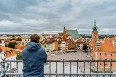Royal Castle, Castle Square ve Old Town, Varşova, Poland 'ın çatı manzarasının tadını çıkaran bir gezgin. Bulutlu bir günde tarihi şehir merkezine bakan bir turist. Şehir içi anorama. Seyahat kentsel konsepti.