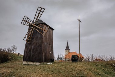 Vrbice, Çek Cumhuriyeti, Moravya 'da şarap köyü, geleneksel ahşap yel değirmeni ve şarap fıçısı, arka planda kilise. Şarap tatma, yerel halk. Bulutlu bir günde Çek kırsalında.