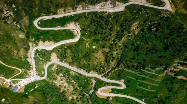 Winding road from high mountain pass in Dolomites, Italy. Great road trip through dense woods and meadows. Aerial view. Curvy road in summer forest scenery, mountain landscape.Top Down Birds Eye View