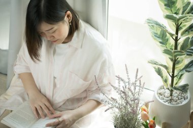 Oturma odasında kitap okuyan Asyalı kadınla hala ev kavramında.