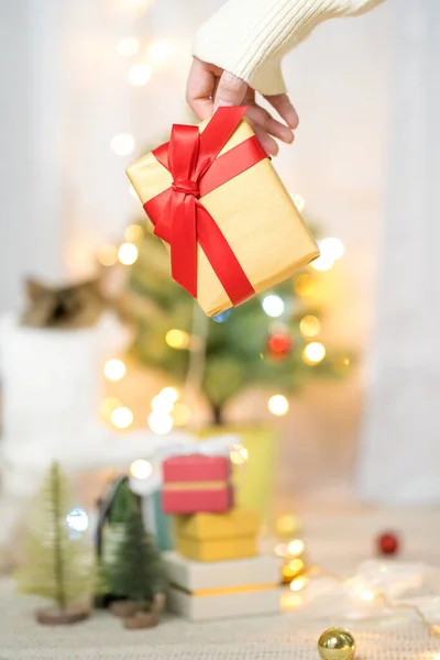 クリスマスツリーの背景を持つ女性の手は新年のギフトボックスを保持 — ストック写真