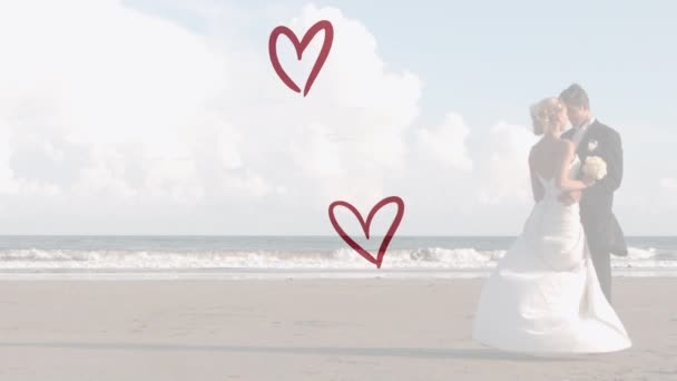 結婚式の服を着てビーチでキスをする白人カップルの上に赤い心のアニメーション 婚約恋愛愛の概念をデジタルで生成したビデオ — ストック動画