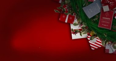 Kırmızı parçacıklar Noel çelengi süslemesi ve kırmızı arka planda hediyeler üzerine düşüyor. Noel şenliği ve kutlama konsepti