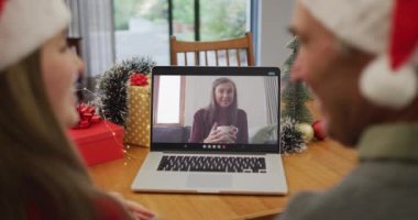 Noel Baba şapkası takan beyaz bir çiftin Noel 'de dizüstü bilgisayarda görüntülerini izliyoruz. Noel zamanı covid 19 salgınında sosyal mesafeler