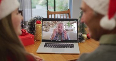 Noel Baba şapkası takan beyaz bir çiftin Noel 'de dizüstü bilgisayarda görüntülerini izliyoruz. Noel zamanı covid 19 salgınında sosyal mesafeler