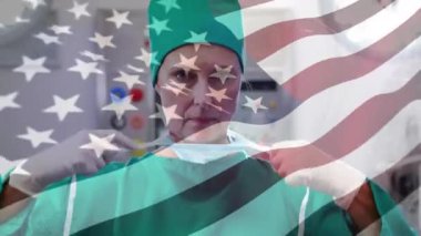 Amerikan bayrağının maskeli bir cerrahın üzerinde dalgalanması. küresel covid 19 salgın hastalık ve sağlık hizmetleri konsepti dijital olarak oluşturulmuş video.