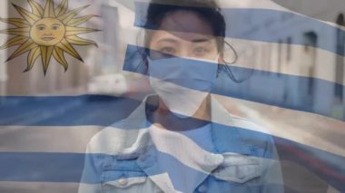 Uruguay bayrağının covid 19 salgını sırasında yüz maskesi takan kadının üzerinde dalgalanması. küresel covid 19 salgın konsepti dijital olarak oluşturulmuş video.